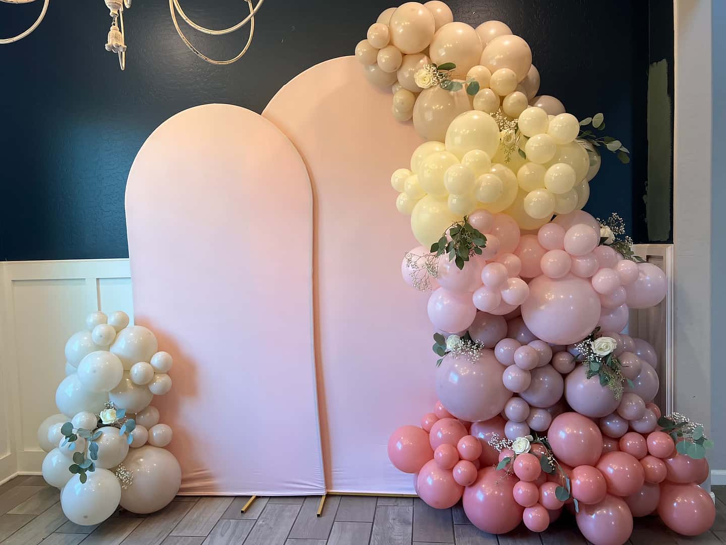 Pastel balloon garland in blush, butter yellow, and soft pink with white roses and eucalyptus on a blush double-arch backdrop for a bridal shower